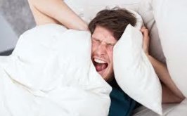 Man trying to sleep holding pillows over ears and shouting